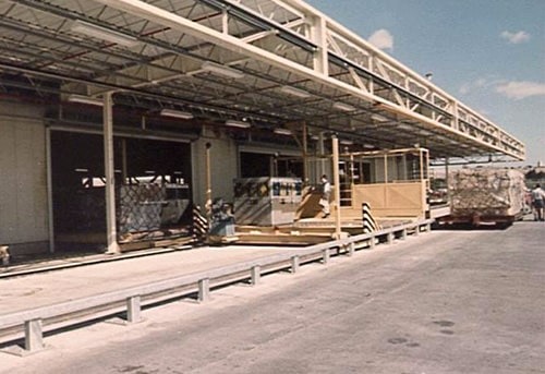A bustling 1970s airport terminal with glass walls, metal beams, and a tarmac visible.