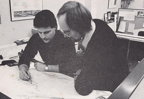 Two people collaborating on a drafting project, with one person pointing and the other taking notes.