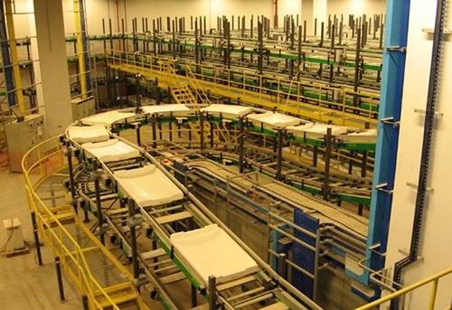 An industrial production facility with rows of machinery, conveyors, and storage shelves.