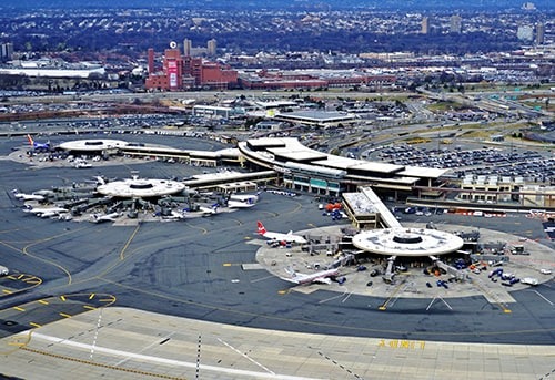 Aerial view of bustling Port Authority airport with planes, terminals, and cityscape in the background.