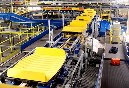 An automated production line with yellow equipment and conveyors transporting various items in a large industrial facility.