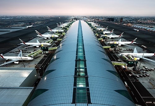 Aerial view of Dubai International Airport with runways, terminals, and aircraft.