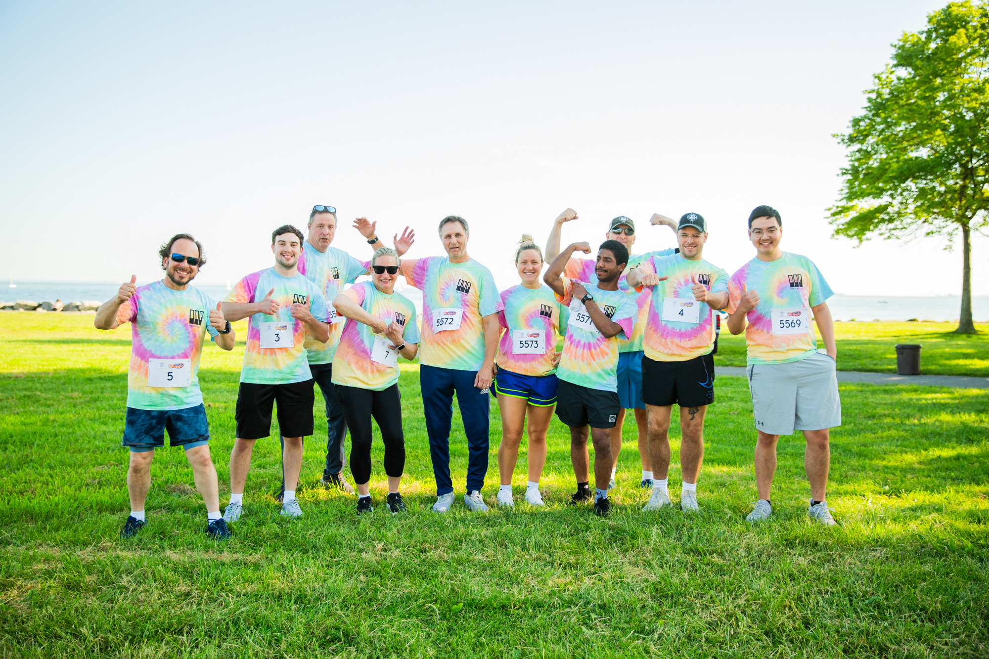 Group of people wearing colorful tie-dye shirts standing together on a grassy field.