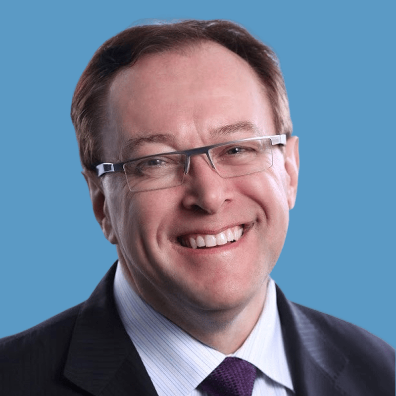 Smiling middle-aged man with glasses and a suit, against a blue background