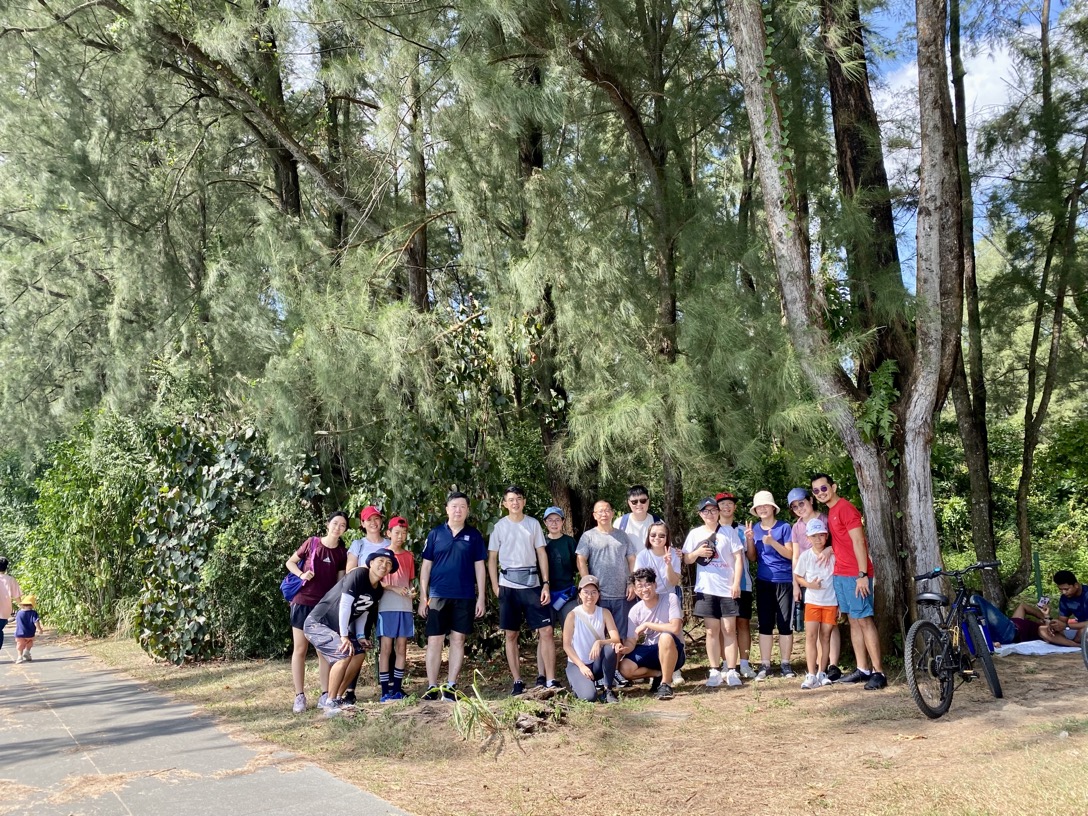 Group of people in casual attire posing together in a lush, wooded park setting on Singapore National Day.