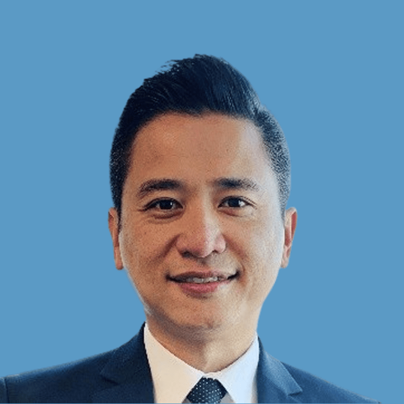 Smiling Asian man in a suit and tie against a blue background.