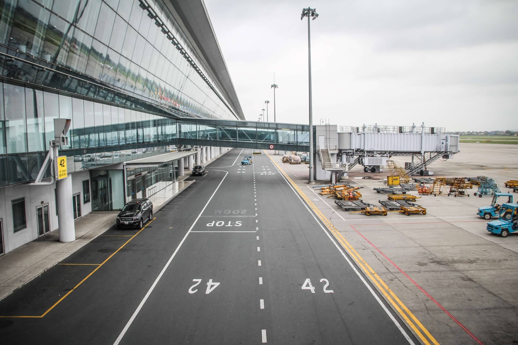 Glass airport terminal with jet bridges, service vehicles, and numbered parking spots visible.